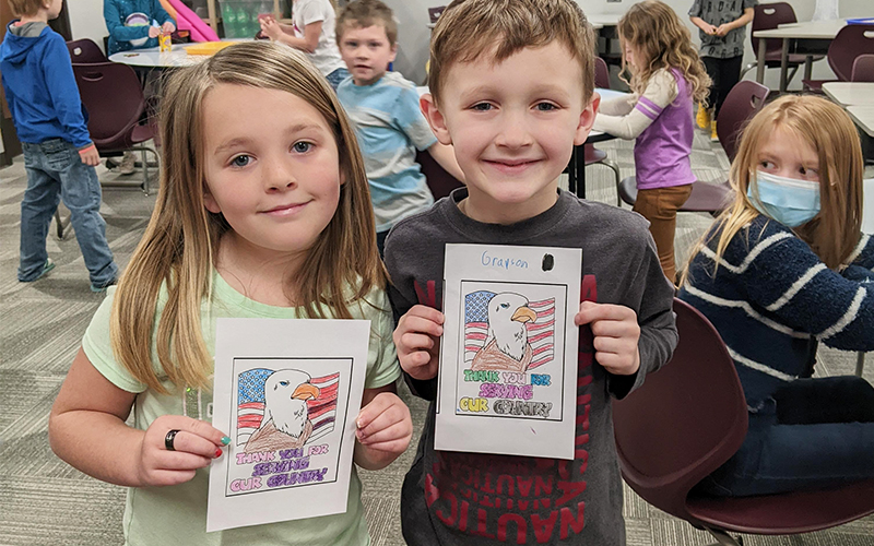 Two happy elementary students holding up thank you for serving our country coloring sheets